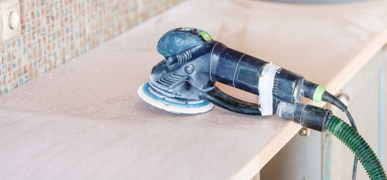 Repairing solid surface countertops in kitchen. Orbital sander tool used to repair stone countertops set on cabinet base.