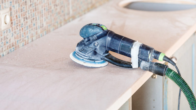 Repairing solid surface countertops in kitchen. Orbital sander tool used to repair stone countertops set on cabinet base.