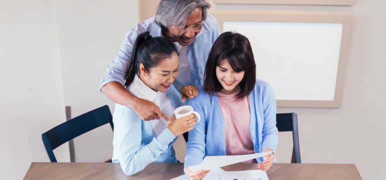 Happy Asian couple reading a home offer letter from prospective home buyers with their real estate agent.