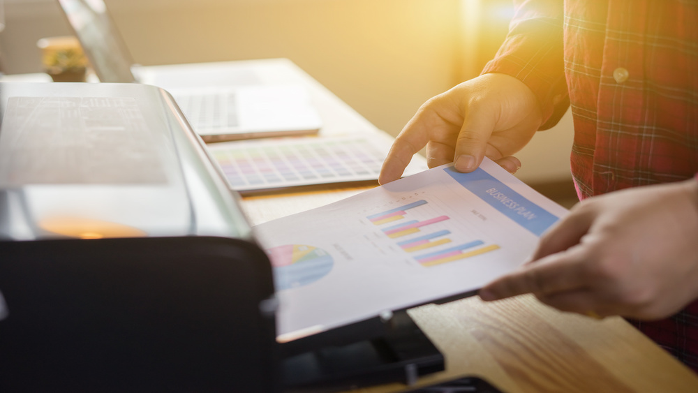 Businessman analyzing investment charts and business plan with printer.