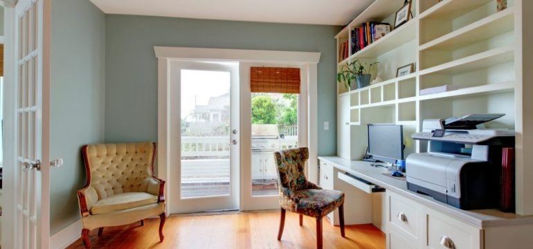 Living room converted to a home office with green walls and white shelves.