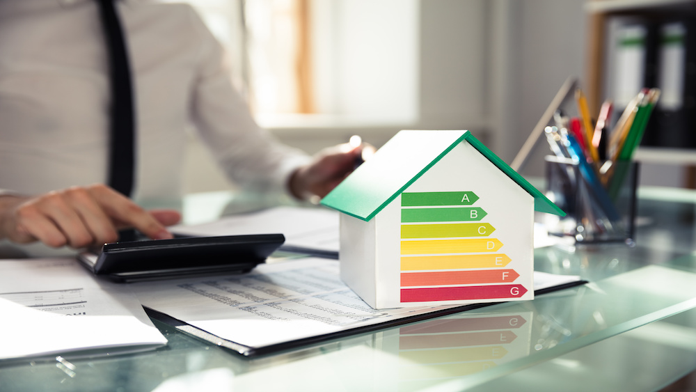 Close-up of a house model showing energy efficiency rate after a home energy audit In front of a businessperson's hand using a calculator.