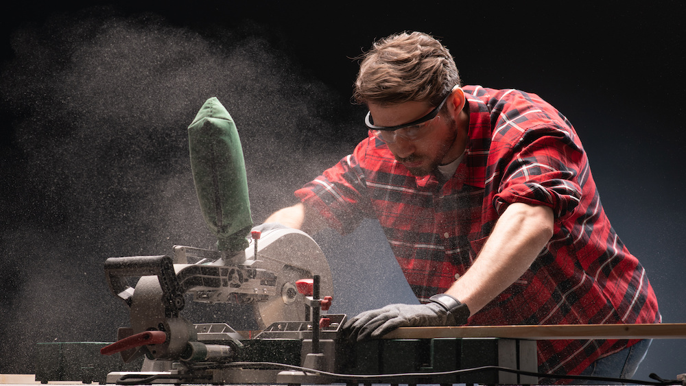 A male carpenter using modern electric circular saw for cutting wood a workshop to show an example of workbench tools.