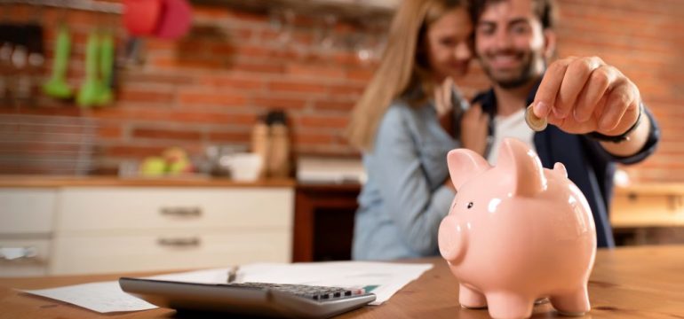 Happy millennial couple inserting coin in piggybank. Home down payment budget, family finance concept.