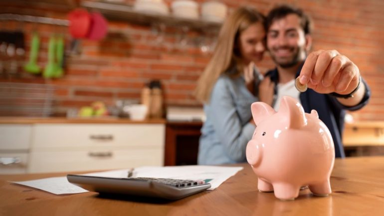 Happy millennial couple inserting coin in piggybank. Home down payment budget, family finance concept.