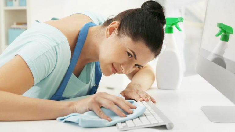 Young woman trying to carefully clean computer keyboard in her home office.