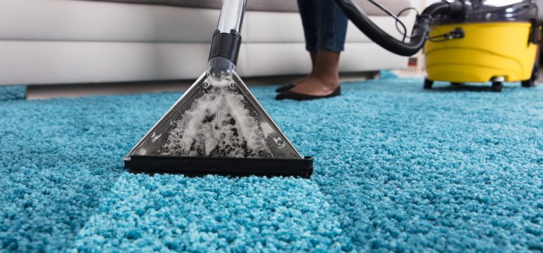 Person using vacuum cleaner for deep cleaning blue wall-to-wall carpets in a home.