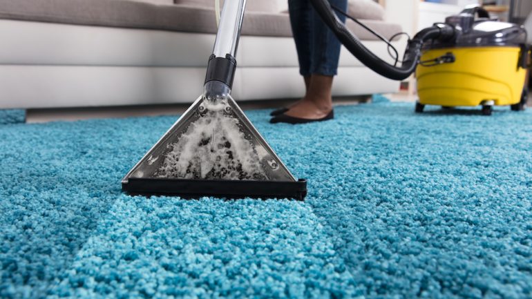 Person using vacuum cleaner for deep cleaning blue wall-to-wall carpets in a home.