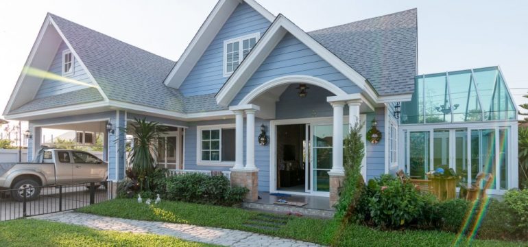 Bright blue house with no garage in sun light with colorful poppies and some graceful trees.