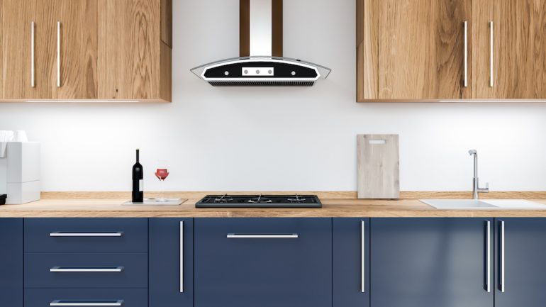 Close up of blue kitchen cabinets with built in stove top, sink, and wooden cupboards above them.