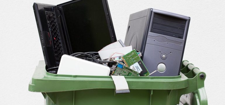 Green waste can filled with computers for electronics recycling and disposal.