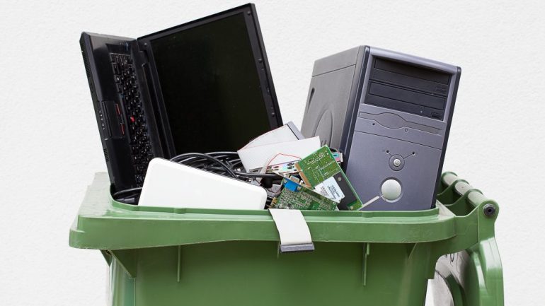 Green waste can filled with computers for electronics recycling and disposal.