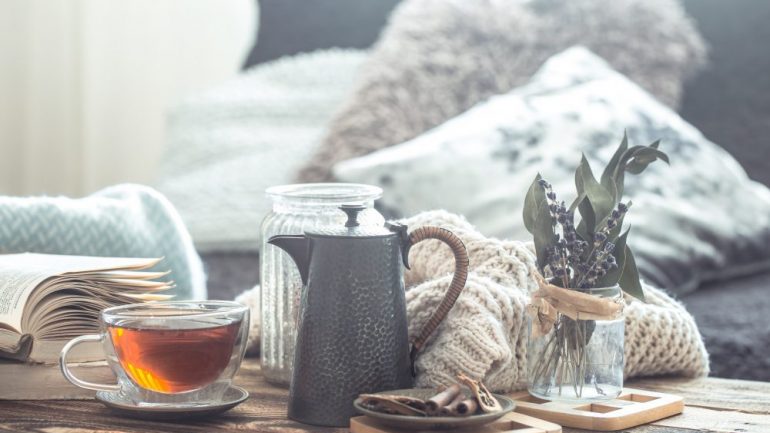 Still life details of home cool-season decor on a wooden table with a cup of tea. Shows the concept of cool season coziness and home atmosphere.