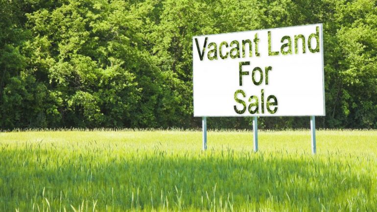 Billboard in green grass advertising rural land for sale.