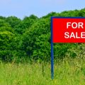 Concept of buying land with a real estate agent. Photo of rural land with a red for sale sign on the property.