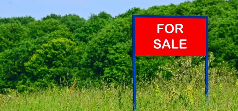 Concept of buying land with a real estate agent. Photo of rural land with a red for sale sign on the property.