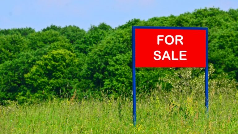 Concept of buying land with a real estate agent. Photo of rural land with a red for sale sign on the property.