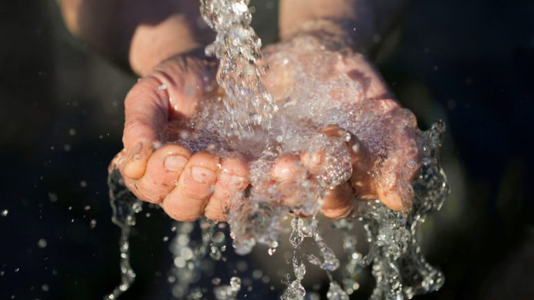 Hands washing with well water pouring from a spigot.