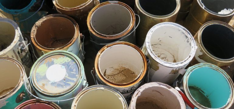 Leftover paint in cans on the floor of a storage room.