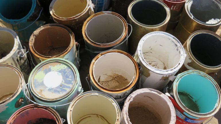 Leftover paint in cans on the floor of a storage room.