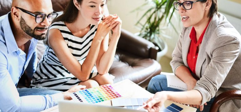 Pretty middle-aged interior decorator sharing ideas with her clients while having meeting in cozy boardroom, they listening to her with interest.