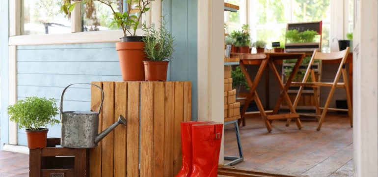 A She Shed with rubber boots, watering can and plants on wooden crates near door.