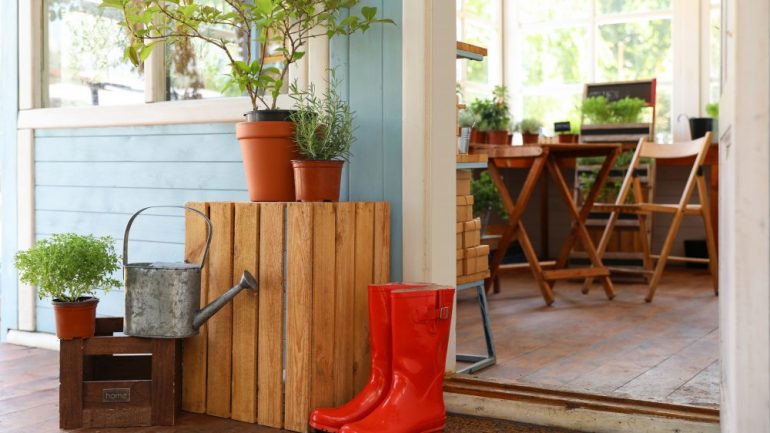A She Shed with rubber boots, watering can and plants on wooden crates near door.