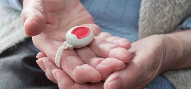 Senior citizen holding a medical alert device in their hands.