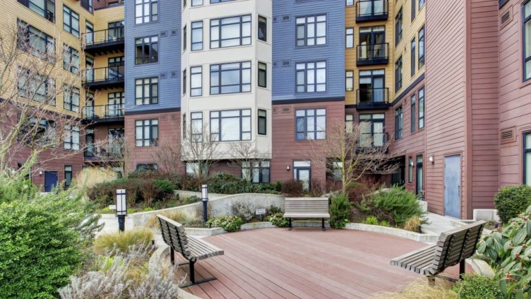 Empty benches near a ground-floor apartment in a urban, multi-unit building with several floors.