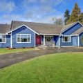 Beautiful rambler house with blue siding and covered porch with double red front door and concrete driveway on a large lot. Shows the buyer's decision to purchase a large lot size versus house size.