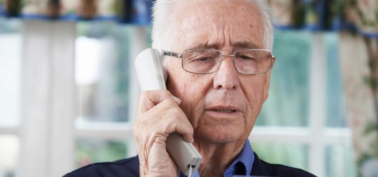 Senior man giving credit card details on a landline phone to a fraudulent robocall.