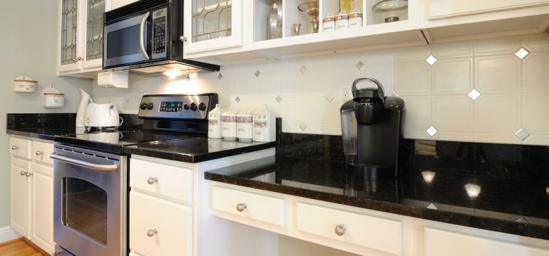 White kitchen cabinets with black counter tops showing kitchen desk area with a coffee maker.
