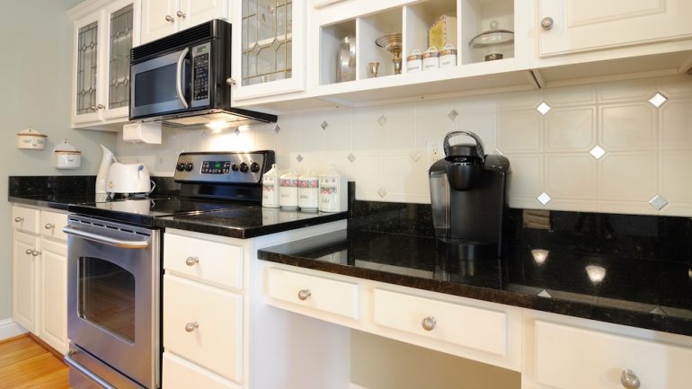 White kitchen cabinets with black counter tops showing kitchen desk area with a coffee maker.