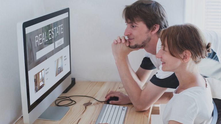 A couple conducting a online home search on a real estate portal on their home desktop computer.