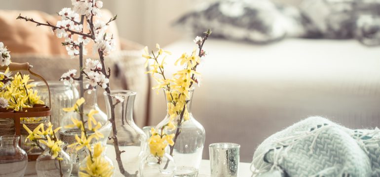 Still-life. Home decor for warmer months. Living room interior design details include vases with spring flowers, on the background of a wooden table.