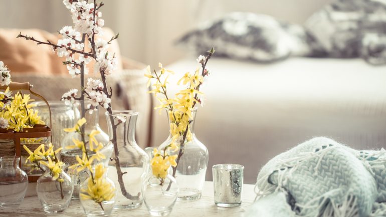 Still-life. Home decor for warmer months. Living room interior design details include vases with spring flowers, on the background of a wooden table.