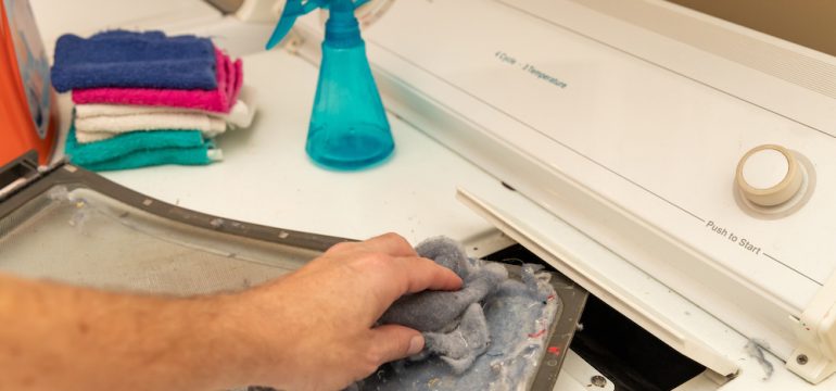 Man's hand removing dirty lint screen of dryer while doing laundry to prevent dryer fires.