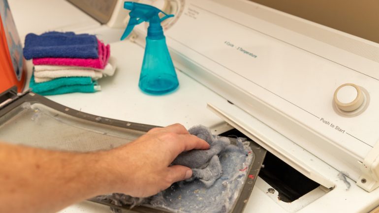 Man's hand removing dirty lint screen of dryer while doing laundry to prevent dryer fires.