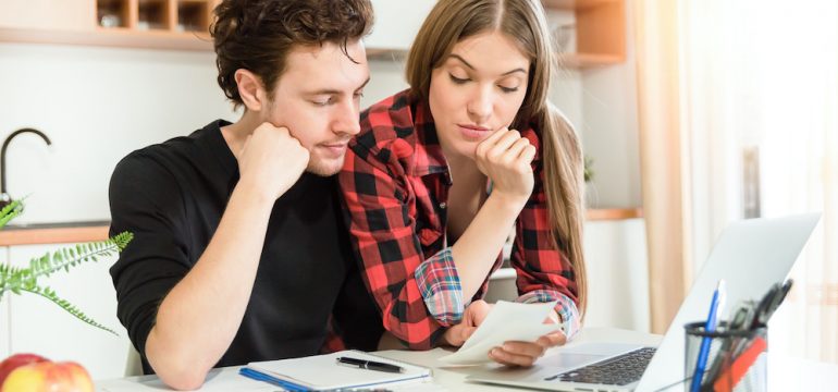 Young couple at home with calculator and bills budgeting during the coronavirus pandemic.