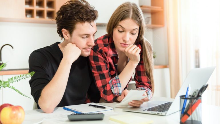 Young couple at home with calculator and bills budgeting during the coronavirus pandemic.