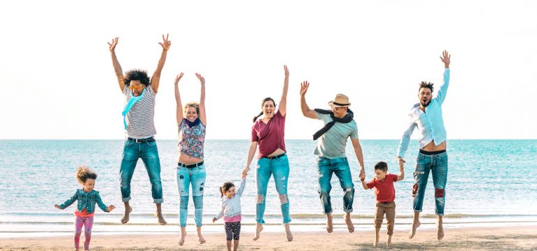 Happy multiracial families jumping together at beach holding hands at their summer vacation home on the beach.