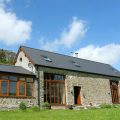 Newly converted residential barndominium with a slate roof in rural countryside against a blue sky with clouds.