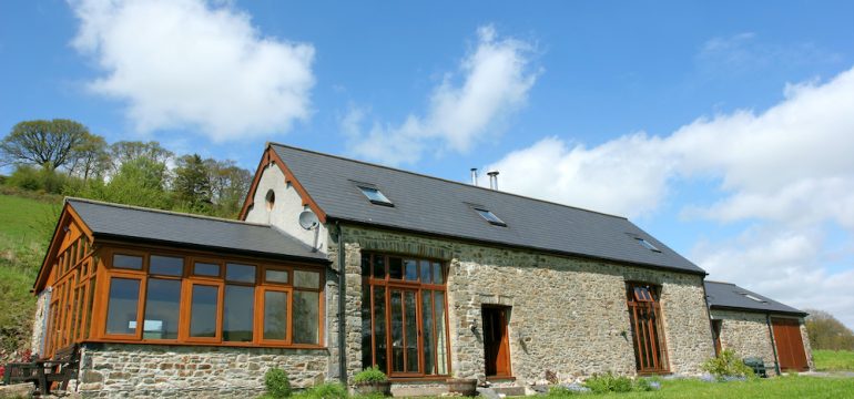Newly converted residential barndominium with a slate roof in rural countryside against a blue sky with clouds.