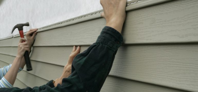 Workers installing home siding holding hammer and nail.