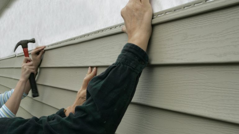 Workers installing home siding holding hammer and nail.