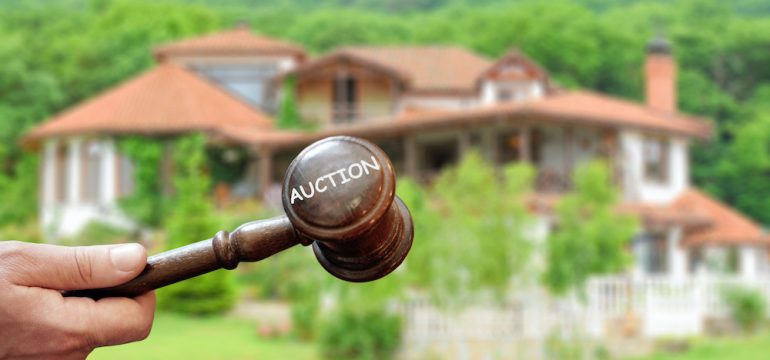 Concept real estate auction,blurred house background and wooden gavel in a hand.