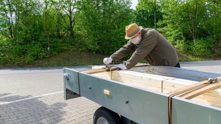 Home service contractor secures the load on his car trailer, wears a breathing mask for protection against the COVID-19 pandemic.