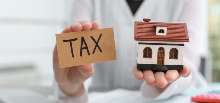 Woman holding house model and card with word TAX. Presents the concept of a tax lien on a house.