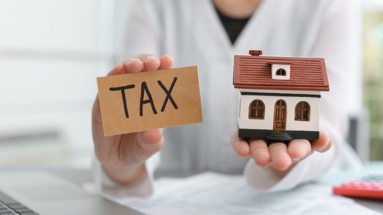 Woman holding house model and card with word TAX. Presents the concept of a tax lien on a house.