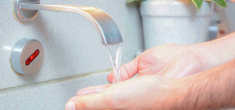 Using a touchless faucet to wash hands in sink.